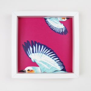 Peut inclure: Un cadre blanc avec un fond rose et deux oiseaux bleus et blancs en vol. Les oiseaux sont stylis&eacute;s et ont un aspect fantaisiste.