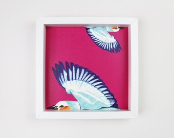 May include: A white frame containing a pink background with two stylised blue and white birds in flight. The birds have a whimsical feel.