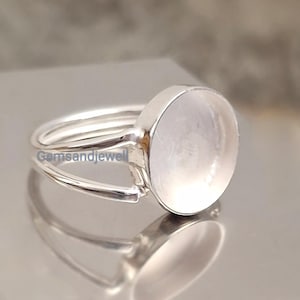 Könnte beinhalten: Ein silberner Ring mit einem großen, runden, hellen Edelstein. Der Ring hat ein Doppelband-Design und der Text "Gemsandjewell" ist auf dem Band sichtbar. Der Edelstein ist in einer Lünettenfassung gefasst.