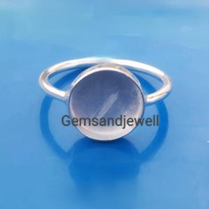 May include: A silver ring with a light blue round gemstone. The ring is on a blue background. The text "Gemsandjewel" is visible on the image.