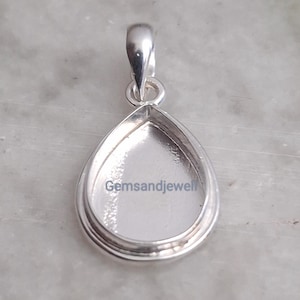 May include: A silver pendant with a teardrop-shaped bezel, designed for a gemstone. The pendant has a loop at the top for a chain. The text "Gemsandjewell" is visible on the face of the pendant.