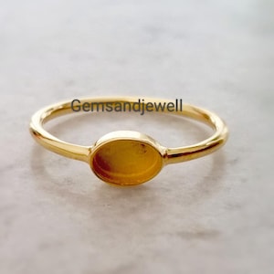 May include: A gold ring with an oval setting. The ring is set against a light-coloured background. The text "gemsandjewell" is visible on the top of the ring.