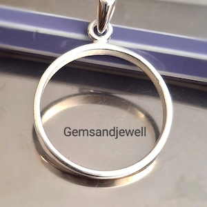 May include: A silver-colored pendant with a circular design and a loop at the top for a chain. The pendant has the text "Gemsandjewell" on the front. The pendant is on a reflective surface.