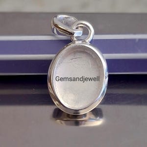 Op de afbeelding: Een zilverkleurige hanger met een ovale zetting. De hanger heeft een lus aan de bovenkant voor een ketting. De tekst "Gemsandjewell" is zichtbaar op de hanger.