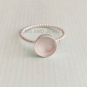 May include: A silver ring with a round bezel setting. The ring band is twisted and has a polished finish.