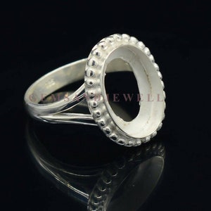 May include: Silver ring with a bezel setting for an oval shaped stone. The ring has a beaded edge around the bezel setting.