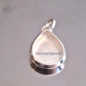 Könnte beinhalten: Ein silberfarbener Anhänger mit tropfenförmiger Lünette. Der Anhänger hat oben eine Schlaufe für eine Kette. Der Text "Gemsandjewell" ist auf den Anhänger gedruckt. Der Anhänger ist reflektierend.