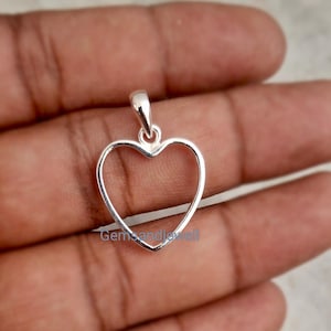 Puede incluir: Un colgante plateado en forma de corazón con un lazo para una cadena. El colgante tiene un diseño simple y abierto, que destaca un contorno de corazón. La joya es probablemente de plata de ley.