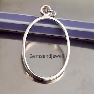 Peut inclure: Un pendentif ovale argenté avec une petite boucle en haut pour une chaîne. Le pendentif a une surface lisse et polie et le texte "Gemsandjewel" est visible sur la surface.