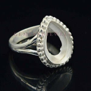 May include: Silver ring with a pear-shaped bezel setting. The bezel is surrounded by a row of small beads.