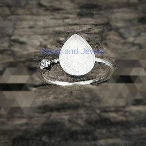 May include: Silver ring with a teardrop-shaped bezel for a stone. The ring has a small clear stone on the side.