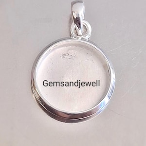 May include: A silver-colored pendant with a circular setting and a loop for a chain. The pendant has the text "Gemsandjewell" printed on the inside. The pendant is designed to hold a gemstone or other decorative element.