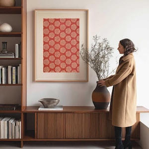 Vintage fabric wall art print with a red floral block print stencil pattern, framed and displayed in a home office beside a bookcase and a woman arranging branches in a clay vase.