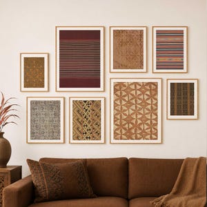 May include: A collection of framed textile art pieces with various patterns and colors. The frames are a light brown color. The patterns include stripes, geometric shapes, and floral designs. The artwork is displayed on a white wall above a brown sofa.