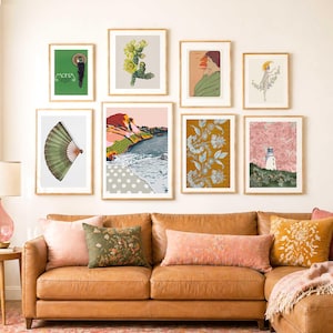 Puede incluir: Una colección de grabados artísticos enmarcados expuestos sobre un sofá de cuero marrón. Los grabados presentan varias ilustraciones, incluyendo estudios botánicos, diseños abstractos y escenas costeras. El sofá está adornado con cojines decorativos en tonos rosa, verde y amarillo.