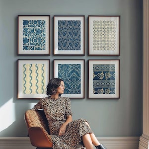 May include: Six framed prints with detailed blue and white patterns adorn a pale blue wall. The prints showcase floral, paisley, and geometric designs. A woman in a leopard print dress is seated in a chair in front of the prints.