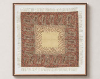 May include: A square textile piece framed in wood, featuring a central cream-coloured square surrounded by a border of intricate red and brown paisley patterns. The entire square is finished with a delicate fringe along all four edges.