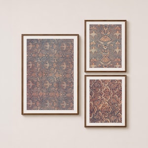May include: Three framed wall art prints featuring intricate batik-style patterns in shades of dark blue and muted orange. The largest print is vertical, while the two smaller prints are stacked on the right, all encased in thin brown wooden frames.