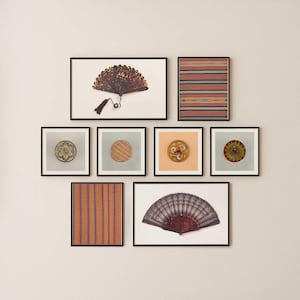 May include: A collection of framed art pieces featuring various designs. The artwork includes a fan with a tassel, striped patterns, and circular decorative elements. The frames are black, and the art pieces are displayed against a white wall.
