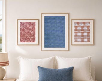 May include: Three framed art prints with floral, woven, and geometric patterns in red, blue, and brown hues. The prints are displayed above a bed with white pillows and a blue lumbar pillow, creating a cohesive bedroom decor.