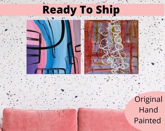 Op de afbeelding: Twee originele abstracte schilderijen op canvas. Het schilderij links is een blauw, roze en paars abstract ontwerp met zwarte lijnen. Het schilderij rechts is een rood, wit en paars abstract ontwerp met witte lijnen. De tekst "Ready To Ship" staat bovenaan de afbeelding. De tekst "Original Hand Painted" staat onderaan de afbeelding.
