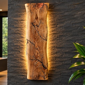 Puede incluir: Un aplique de pared vertical fabricado con una losa de madera natural. La madera presenta patrones fractales oscuros y ramificados en su superficie y emite un brillo cálido y suave desde sus bordes, creando un efecto de retroiluminación.