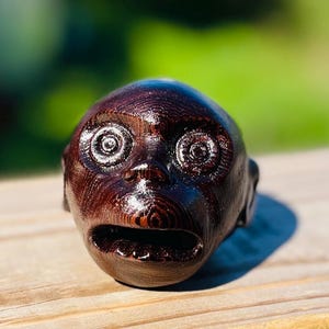 May include: A dark brown wooden sculpture of a face with a wide open mouth and swirling eyes.