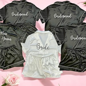 May include: Five black satin pajama sets with short sleeves and shorts. The sets have white embroidery that reads "Bride", "Maid of Honor", and "Bridesmaid".