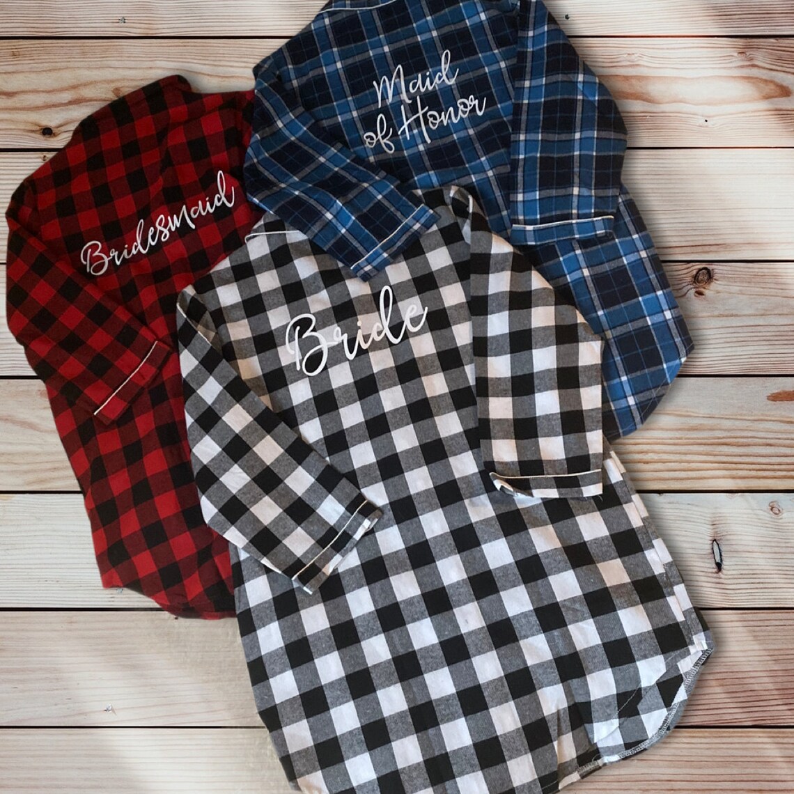 May include: Three flannel pajama shirts in red, black and white buffalo check, and blue plaid.  Each shirt features embroidered text: 'Bridesmaid', 'Bride', and 'Maid of Honor'. The shirts are long-sleeved and have a relaxed fit, perfect for bridal party gifts or slumber party attire.