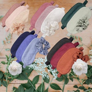 May include: A collection of satin sleep masks and scrunchies in shades of pink, white, navy, and rust. The masks are displayed on a wooden surface with floral decorations, highlighting the different colours and textures.
