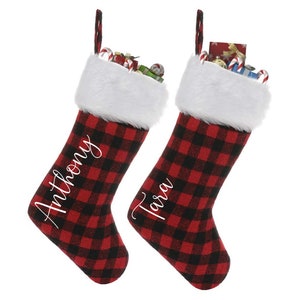 May include: Two red and black buffalo plaid Christmas stockings with white faux fur trim. The stockings are personalized with the names "Anthony" and "Tara" in white script.