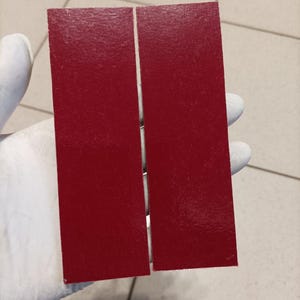 May include: Two rectangular pieces of red material, side by side, with a textured surface. The material is a deep, rich red color. The pieces are held by a gloved hand.