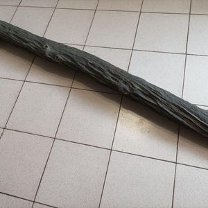 May include: A weathered, dark gray wooden log with a textured surface. The log is long and cylindrical, with visible knots and grooves, suggesting natural aging. It rests diagonally on a tiled surface.