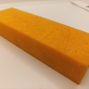Può includere: Un blocco rettangolare di materiale arancione solido con una superficie strutturata. Il blocco è di una vibrante tonalità arancione e sembra essere fatto di un materiale denso e solido. I bordi sono puliti e ben definiti, suggerendo che potrebbe essere un materiale artigianale o da costruzione.