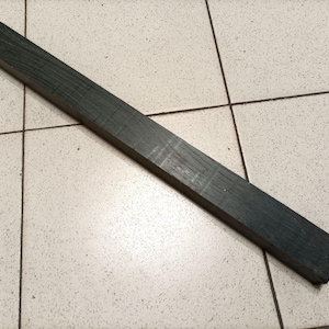 May include: A long, dark green wooden dowel rod with a slightly rough texture.
