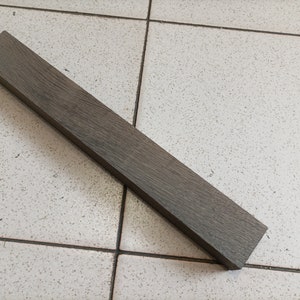 May include: A dark gray wooden dowel rod, approximately 12 inches long, with a smooth, slightly textured surface.