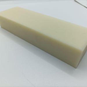 以下が含まれることがあります： 淡いベージュ色の長方形のブロック。石鹸または同様の固形物である可能性があります。 ブロックは滑らかで均一な色をしており、エッジとコーナーが見えます。白い表面に置かれています。
