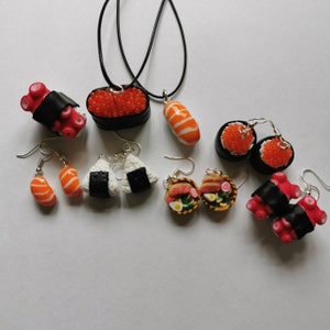 K&ouml;nnte beinhalten: Ein Set an Sushi-Schmuck, bestehend aus Ohrringen und einer Halskette. Die Ohrringe zeigen verschiedene Sushi-Rollen, darunter Lachs, Thunfisch und Avocado. Die Halskette zeigt eine Sushi-Rolle mit einem schwarz-wei&szlig;en Design. Der Schmuck ist aus Polymer Clay gefertigt und perfekt f&uuml;r Sushi-Liebhaber.