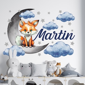 May include: A nursery wall decal featuring a cute orange fox sitting on a crescent moon with blue clouds and stars. The name "Martin" is written in a whimsical font.