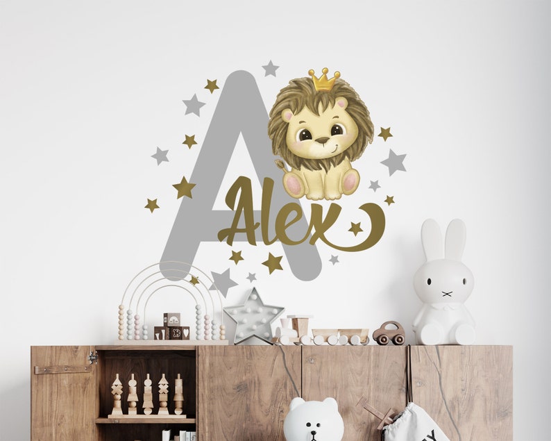 May include: A gray letter A with gold stars and a gold crown on top. A cute cartoon lion wearing a gold crown is sitting on the letter. The name Alex is written in gold letters below the lion.