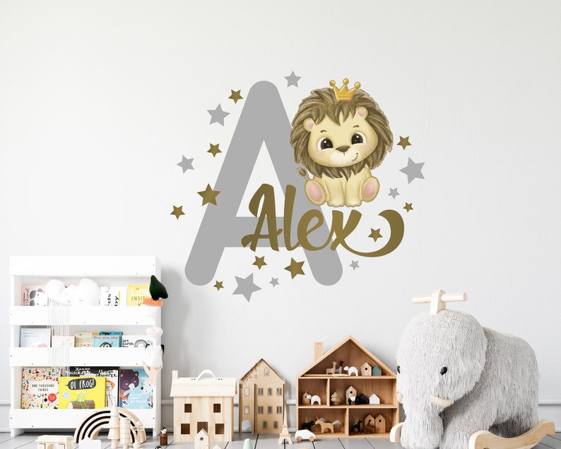 May include: A gray and gold wall decal featuring a lion wearing a crown, the letter A, and the name Alex. The decal is surrounded by gold stars.