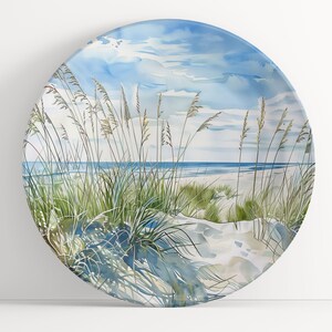 May include: A watercolor painting of a beach scene with tall grasses in the foreground and a blue ocean in the background. The sky is a light blue with white clouds.