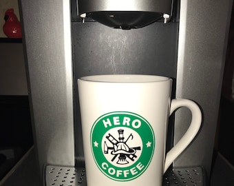May include: A white coffee mug with a green circle logo that says "HERO COFFEE" with a firefighter helmet and tools inside the circle.