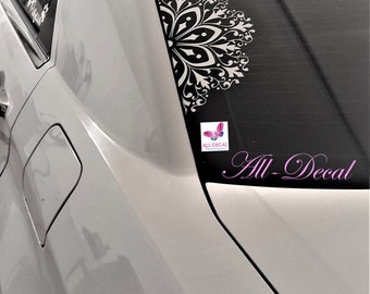 May include: A white car with a black and white mandala decal on the back window. The decal is partially visible and has a floral design. The car also has a pink and white sticker with the text "All Decal" and a butterfly graphic. The text "All Decal" is written in pink cursive on the back window.