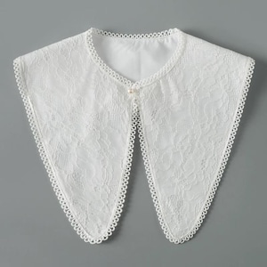 May include: White lace collar with a pearl button in the center. The collar has a pointed shape and a scalloped edge.