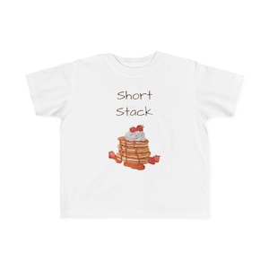May include: White t-shirt with the words "Short Stack" and a graphic of pancakes with cream, strawberries, and syrup. The pancakes are stacked. The shirt is a youth size.