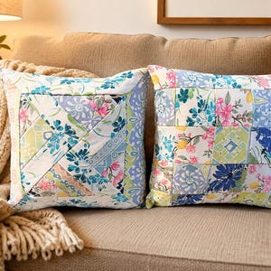 May include: Two square throw pillows featuring a patchwork design with floral and geometric patterns in shades of blue, green, pink, and white. The left pillow has a diagonal strip arrangement, while the right pillow has a grid of square patches.