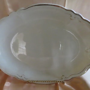 May include: White oval serving platter with a gold rim and delicate floral designs. The platter is made of ceramic and has a glossy finish.