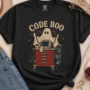 Könnte beinhalten: Ein schwarzes Kurzarm-T-Shirt mit einer Grafik eines Geistes hinter einem roten medizinischen Wagen. Der Geist hält zwei Defibrillator-Paddel. Der Wagen enthält einen Herzmonitor, eine Kaffeetasse und eine Sauerstoffflasche. Der Text CODE BOO ist darüber gedruckt.