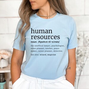 May include: A light blue t-shirt with the words "human resources" in black, along with a definition and a list of related professions. The shirt is made of a soft material.